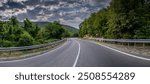 Road landscape forest and mountain. Empty long mountain road to the horizon on a sunny summer day with dramatic cloudy sky. Highway turn panoramic view.