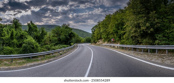 Road landscape forest and mountain. Empty long mountain road to the horizon on a sunny summer day with dramatic cloudy sky. Highway turn panoramic view. - Powered by Shutterstock