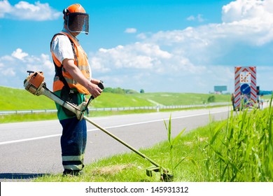 Road landscaper cutting grass along the highway using string lawn trimmer