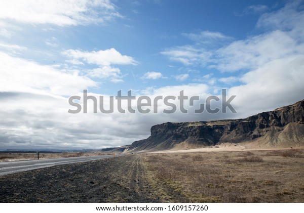 road leading into the distance, blue sky with\
clouds, in the background a\
mountain