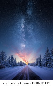 Road Leading Towards Colorful Sunrise Between Snow Covered Trees With Epic Milky Way On The Sky