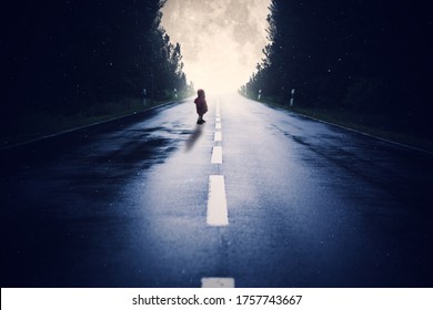 Road leads through the forest during a full moon night. Child stands on the street by full moon
