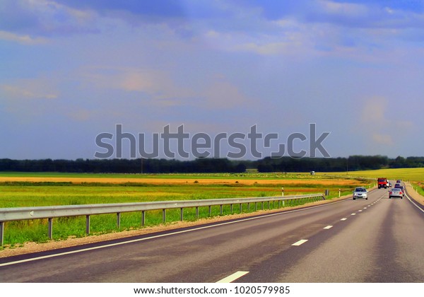 The road leaving into the distance, the turn of\
the road among the blooming field in summer, on a sunny day. Cars\
are driving along the road.
