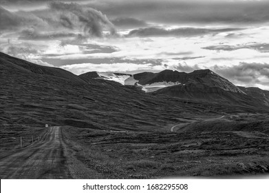 The Road Less Traveled, It's A Mountain Road That Leads Between Akureyri And Siglufjordur, The Sun Is Shining Behind The Cloud Cover And A Car Is Parked By The Road That Snakes Along The Landscape