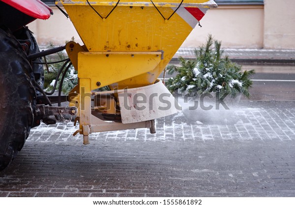 Road maintenance, winter gritter vehicle. Snow\
plow on pedestrian street salting and cleaning road. Tractor\
de-icing street, spreading salt on footpath. Municipal service\
clears street during\
blizzard