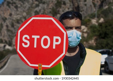 Road Maintenance Worker During The Coronavirus Pandemic, On A Road With A Stop Sign And Reflective Vest