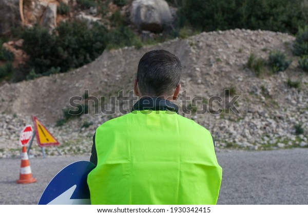 Road maintenance worker\
during the coronavirus pandemic, on a road with a stop sign and\
reflective vest