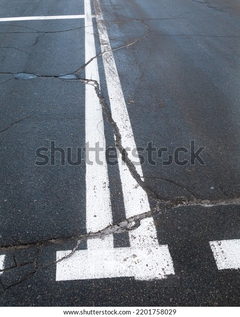 Road with road marking lines. Double
solid white center lines. Cracked asphalt
surface.