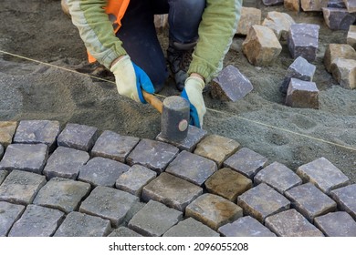 The road master in gloves lays paving stones in layers stone road by professional paver worker