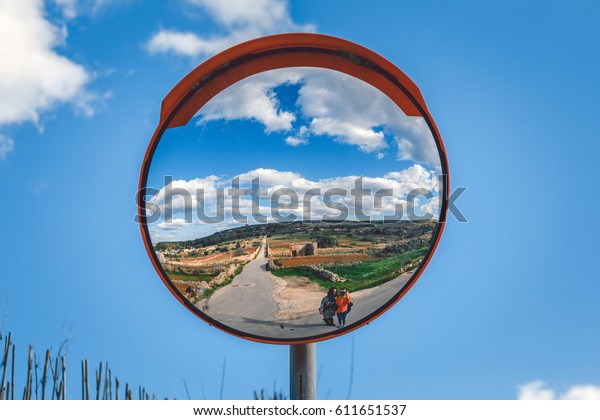 Road mirror. Landscape of Malta with road and two\
girls in street mirror.