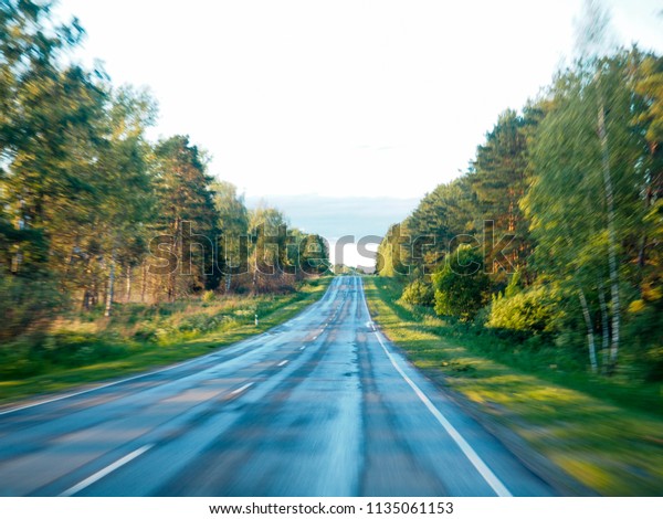 Road in motion blur, Highway in forest in motion\
blur, Open Road in future, no cars, auto on asphalt road through\
green forest, trees, pines, spruces. Clouds on blue sky in summer,\
sunshine, sunny day