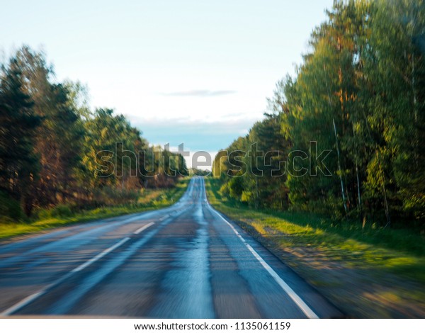 Road in motion blur, Highway in forest in motion\
blur, Open Road in future, no cars, auto on asphalt road through\
green forest, trees, pines, spruces. Clouds on blue sky in summer,\
sunshine, sunny day