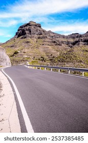A road with a mountain in the background. The road is empty and straight. The sky is blue and clear