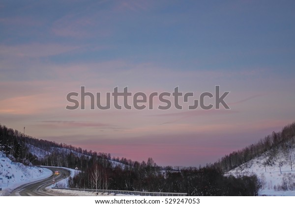 The road in the mountains.\
Pink sunset. The snow cover on the road in the mountains.\
Serpentine in mountains. Cars driving on a winding road in the\
mountains of Altai