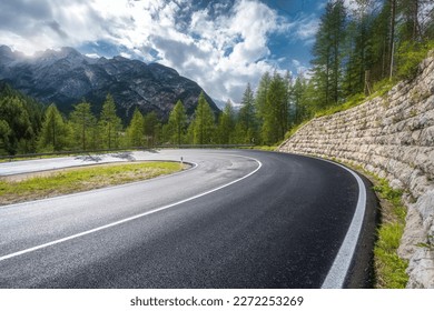 Road in mountains at sunny day in summer. Dolomites, Italy. Beautiful roadway, green tress, high rocks, blue sky with clouds. Landscape with empty highway through the mountain pass in spring. Travel