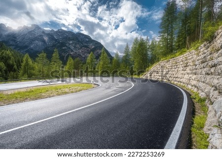 Road in mountains at sunny day in summer. Dolomites, Italy. Beautiful roadway, green tress, high rocks, blue sky with clouds. Landscape with empty highway through the mountain pass in spring. Travel
