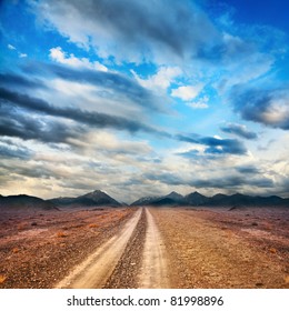 Road To The Mountains Through The Desert At Sky With Clouds