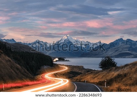 Road to Mt Cook in New Zealand during sunset. Traffic is causing light trails leading to the mountain. 