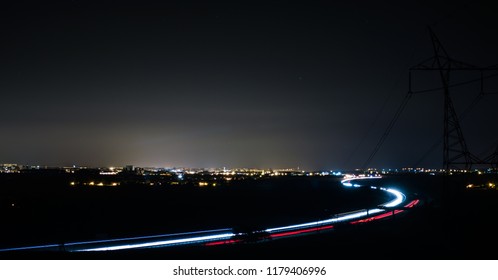 Road At Night Illuminated By Cars With A City In The Distance