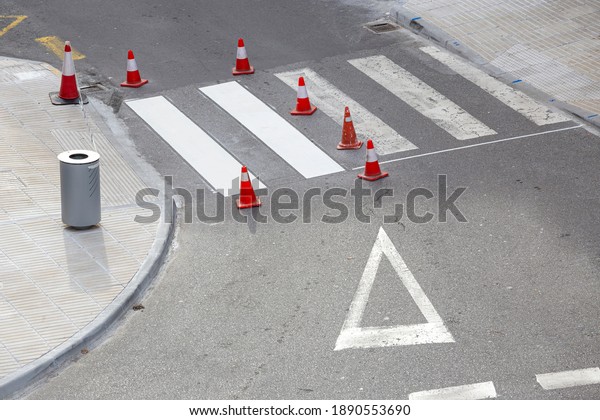 Road painting maintenance concept. Painting white\
street lines on pedestrian crossing and road cones on city. No\
people
