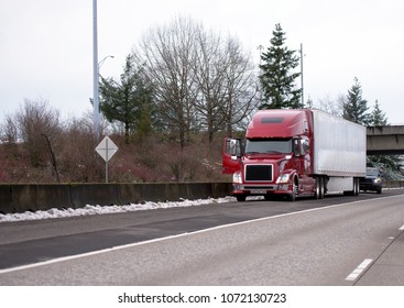 Road patrol police officer checks stopped long-haul red modern big rig semi truck with reefer semi trailer on winter straight interstate multiline highway