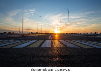 Road with a pedestrian crossing on a new asphalt with a shallow depth of field, blurry background and variable focus. Sunset, warm shades. Road construction concept. Place for text.