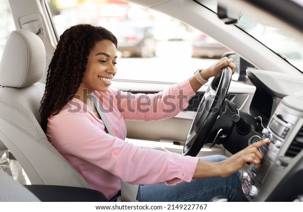 Road Playlist. Side View Profile Portrait Of Happy\
Black Woman Driving Car And Listening To Music On Auto Audio\
System, Checking Automobile Options During Test Drive Pushing\
Button On Turning On Radio