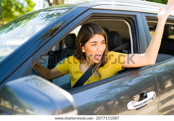 Road rage. Angry and\
aggressive woman shouting to a passing driver while arguing during\
a traffic jam