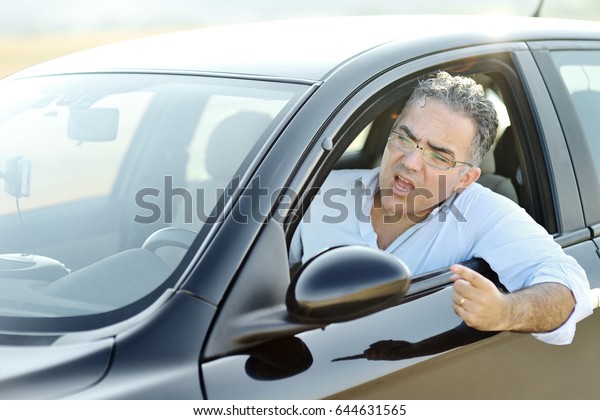 Road rage concept - irritated man screams and\
gestures while driving a black\
car