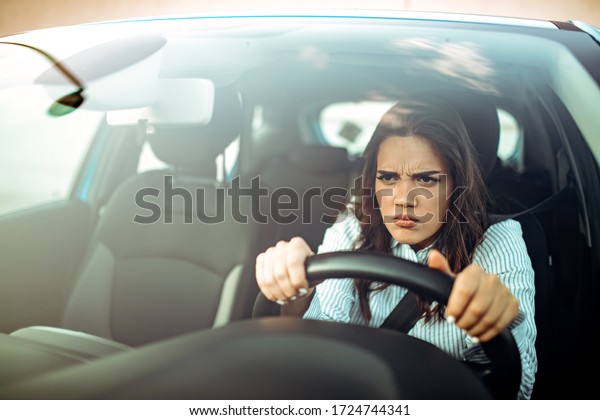 Road rage! Enraged\
young woman driver shouts and points accusingly.  Profile of an\
angry young driver. Negative human emotions face expression. Angry\
woman driving a car