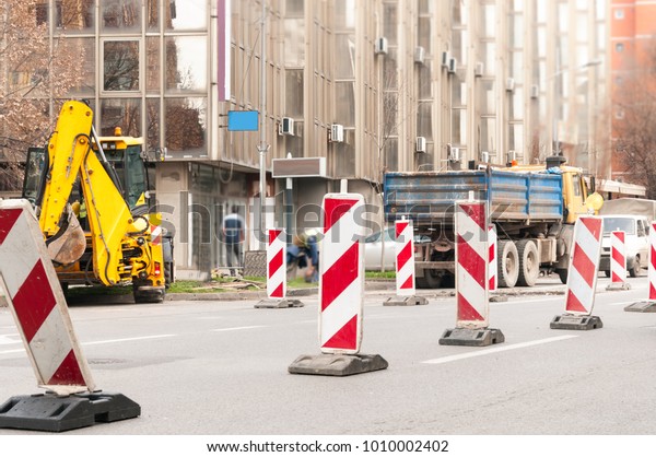 Road reconstruction\
site with traffic barriers excavator constructing loader machinery\
and big heavy truck