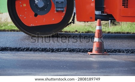 Road roller compacting asphalt during new street paving with traffic cone