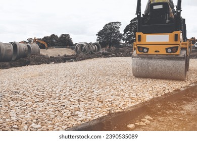 Road roller compacting stone during new road construction in preparation for tarmac, on housing development site