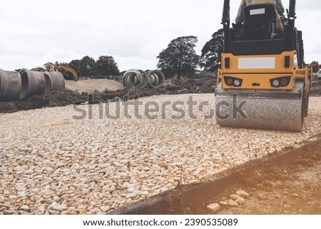 Road roller compacting stone during new road construction in preparation for tarmac, on housing development site