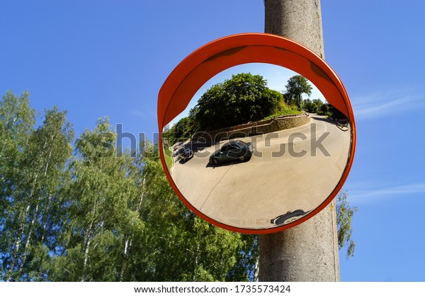 Road round mirror. Mirror to help transport. Help\
cornering. Red round mirror on a post. Road mirror on a background\
of blue sky. Give Way. 