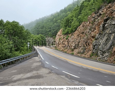 A road running along the side of a large rock side of a mountain along the Cabot Trail.