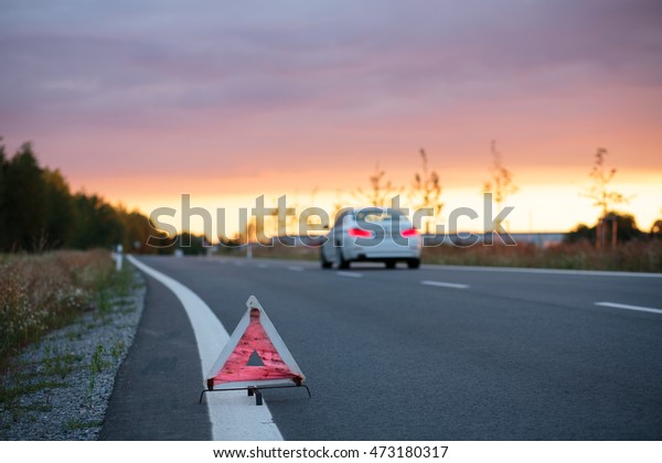 Road safety: emergency road triangle at the side\
of the road at sunset