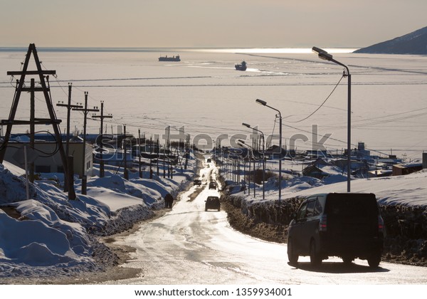 Road to the sea. Cars drive down the street\
towards the sea bay. Cove covered with ice. Among the ice floes\
ships. The end of May in the far North. Nagaev Bay, Magadan,\
Siberia, Far East of\
Russia.