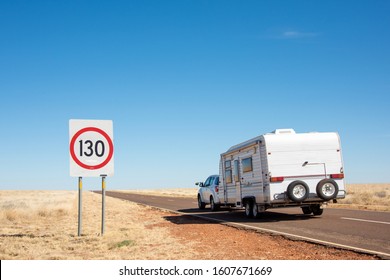 Road showing 130kms/hr sign while car with caravan drives by.