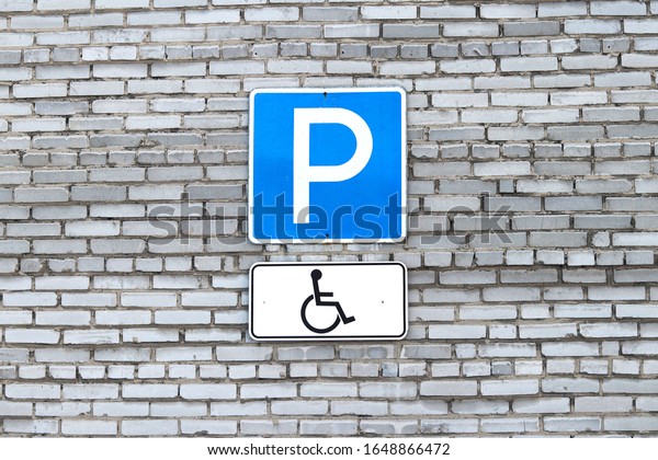 A\
road sign for disabled Parking on a grey brick\
wall.