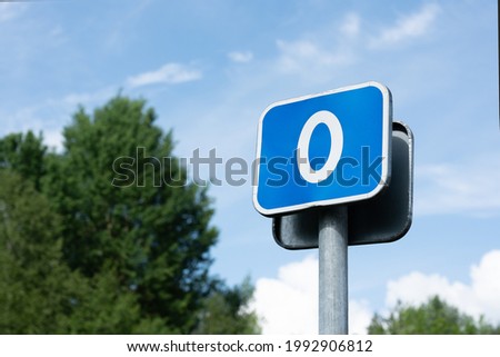 Road sign with the number 0, kilometer zero against the background of a blue sky and blurred trees. The concept of the beginning of the path, the starting point. 