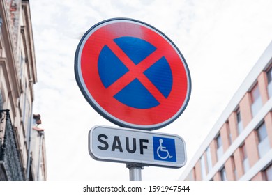 Road sign prohibition of stopping transport, with a white sign and with the inscription in French "except for the disabled" against the background of the apartments of the sleeping area of ​​the city. - Shutterstock ID 1591947544