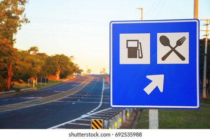 Road Sign At The Roadside Signaling A Gas Station And Food Services On Highway. Blue Board With An Arrow Informing Services Straight Ahead.