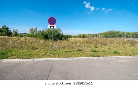 Road sign: "Stopping and Standing Prohibited" on both sides of the sign. In a forest and meadow area.Parking lot (asphalted square) in a secluded forest and meadow area on the outskirts of the city. - Powered by Shutterstock