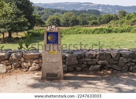The road sign totem with the yellow shell and arrow, that guides the pilgrims along the Camino de Santiago in Galicia, Spain. it shows how many kilometers are left to reach Santiago de Compostela.