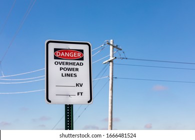 Road Sign Warning Of Overhead Power Lines Danger. Electrical Transmission Wires And Pole In Background