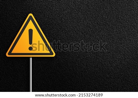 Road sign, yellow triangular shape with exclamation mark on a background of asphalt. Danger signal.
