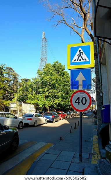 Road signs in the center of Yalta\
in the Crimea, which indicate a speed limit for cars, indicate a\
pedestrian crossing, are located on the sidewalk near the\
house