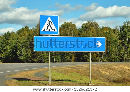 Road signs direction indicator and pedestrian crossing on a road bend, against the sky and forest for information use close-up