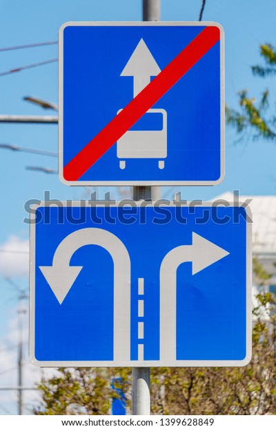 Road signs\
Direction of motion traffic on the lanes closeup against green\
trees and blue sky in sunny\
day